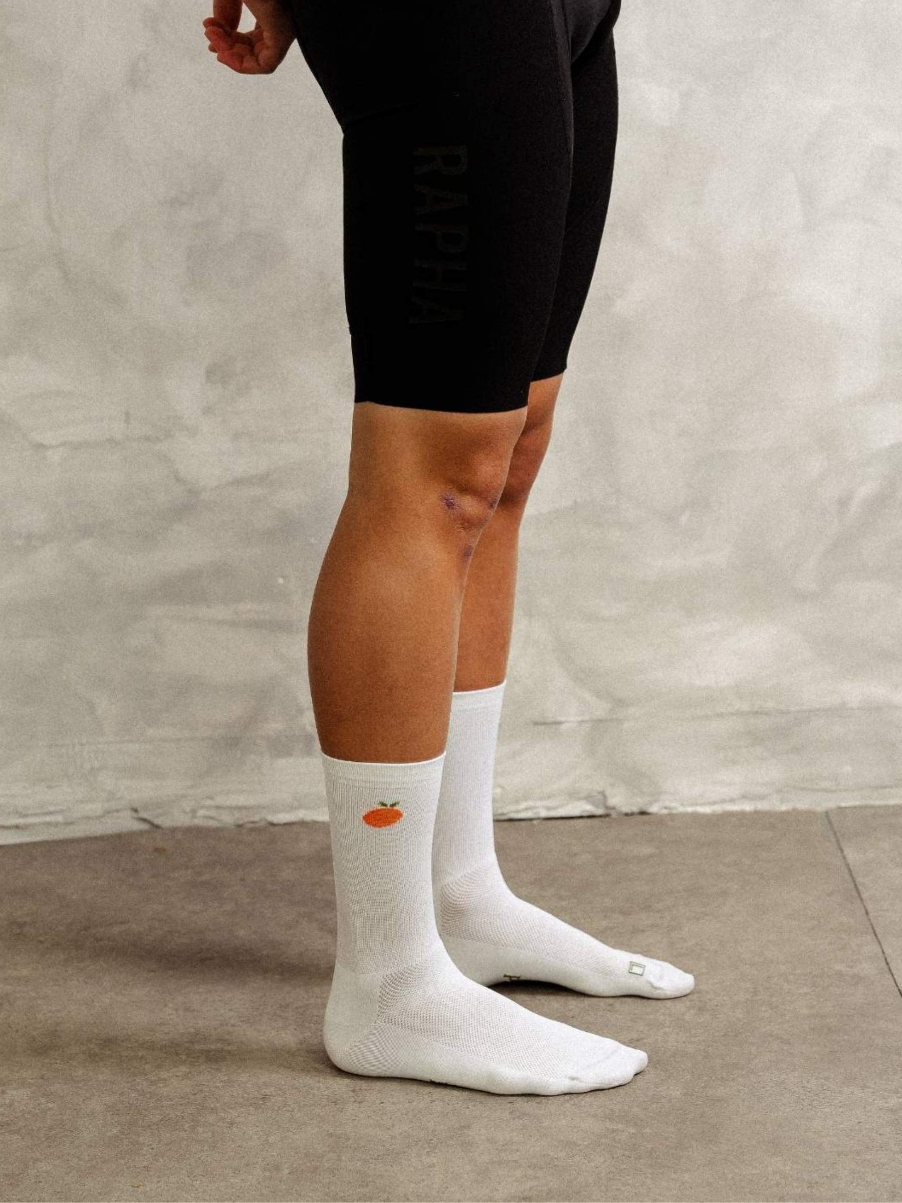 Person wearing white socks with a small orange design on a neutral background