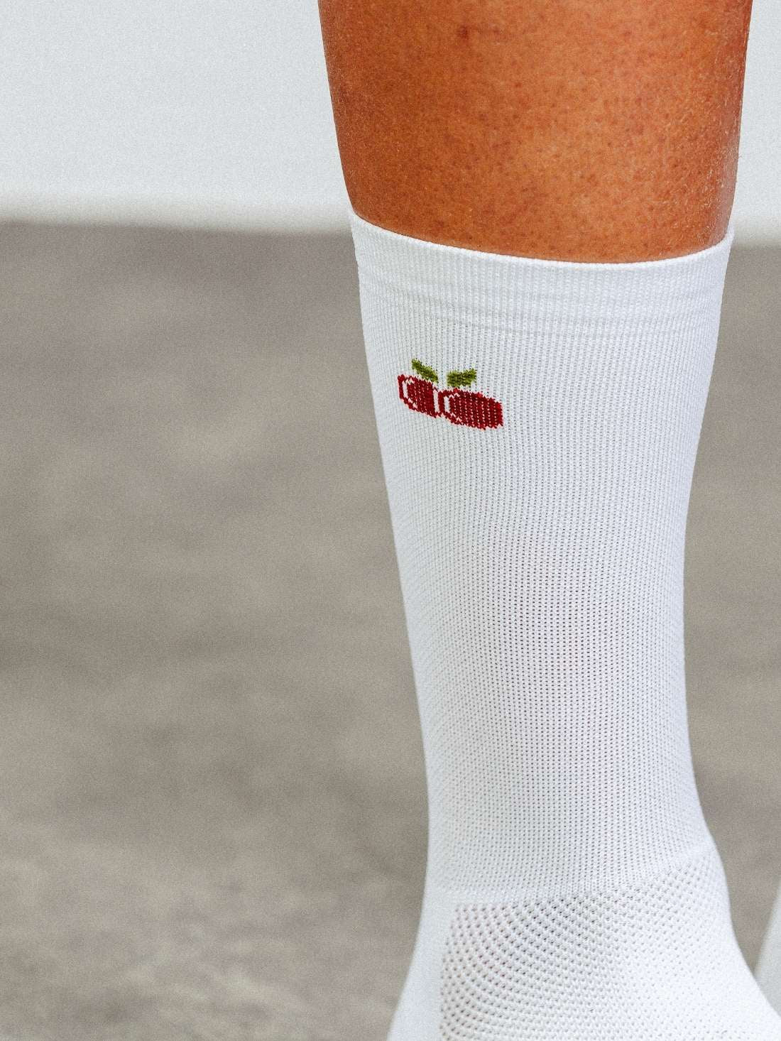 Close-up detail of breathable mesh texture and cherry logo on white performance cycling socks.