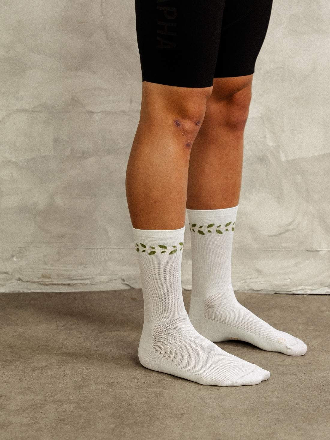 Side profile of cyclist wearing white laurel-patterned socks with 18cm cuff height.