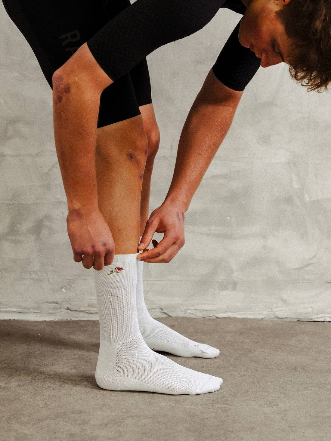 Action shot of cyclist adjusting white performance socks with rose pattern before a ride.