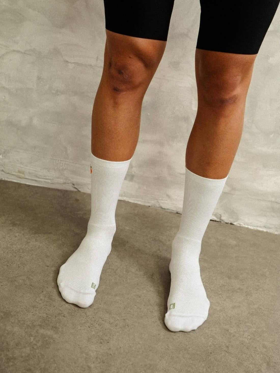 Front view of cyclist's legs wearing white high-performance compression socks with orange fruit design and black cycling shorts.
