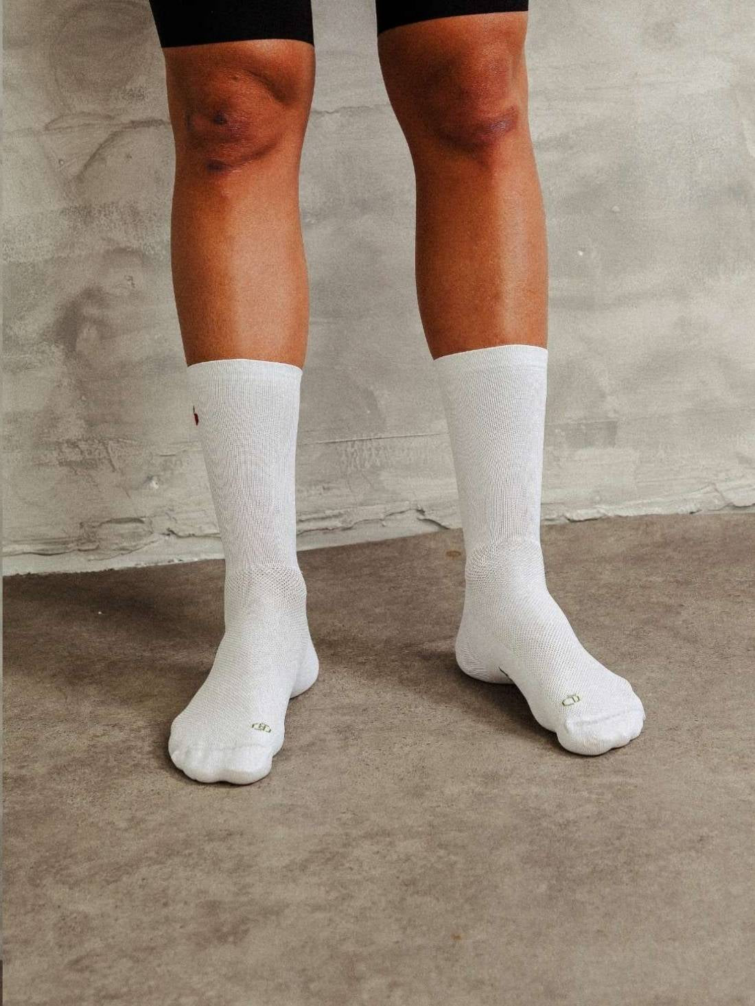Front view of legs wearing white socks with cherry design, showing anatomical fit for road cycling.