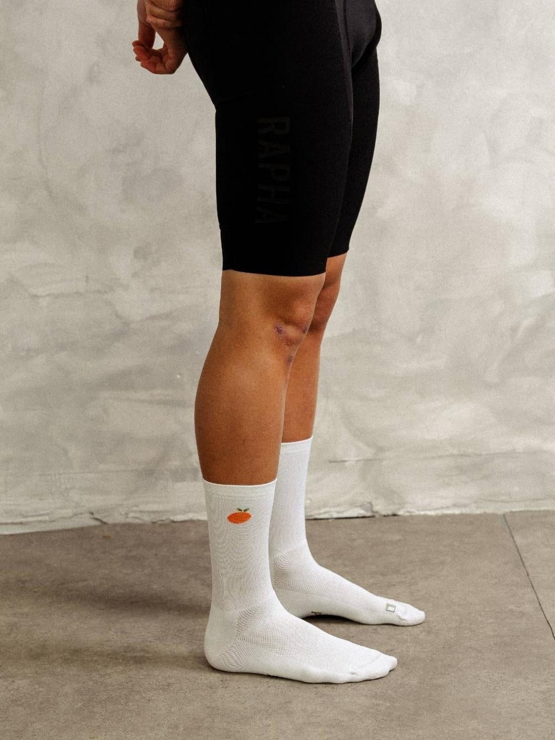 Side profile of adult cyclist wearing white Q-Skin polyamide cycling socks showing 18cm cuff height and fruit logo.