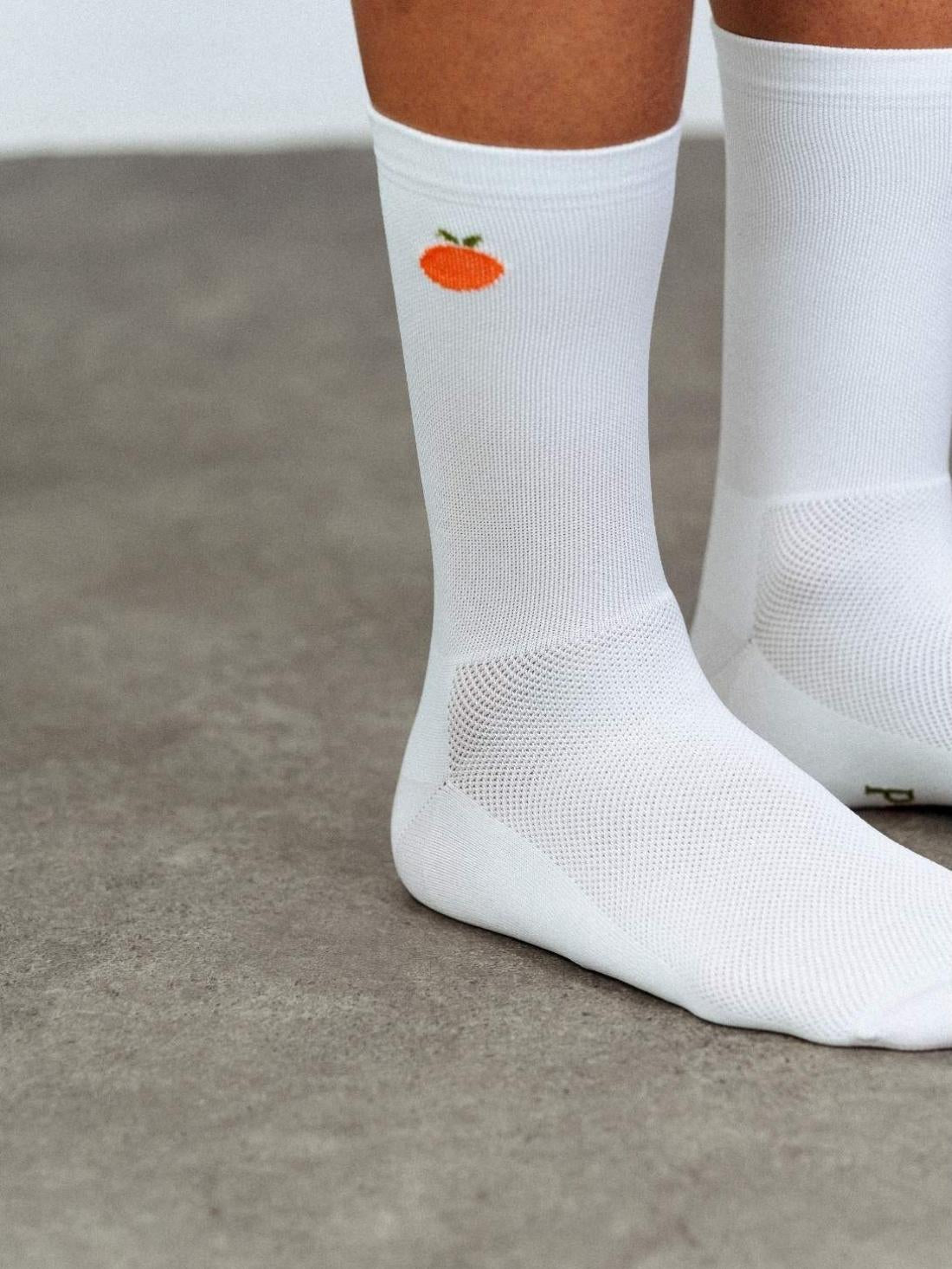 Close-up detail of white high compression cycling sock cuff with small orange fruit pattern and breathable mesh knit structure.